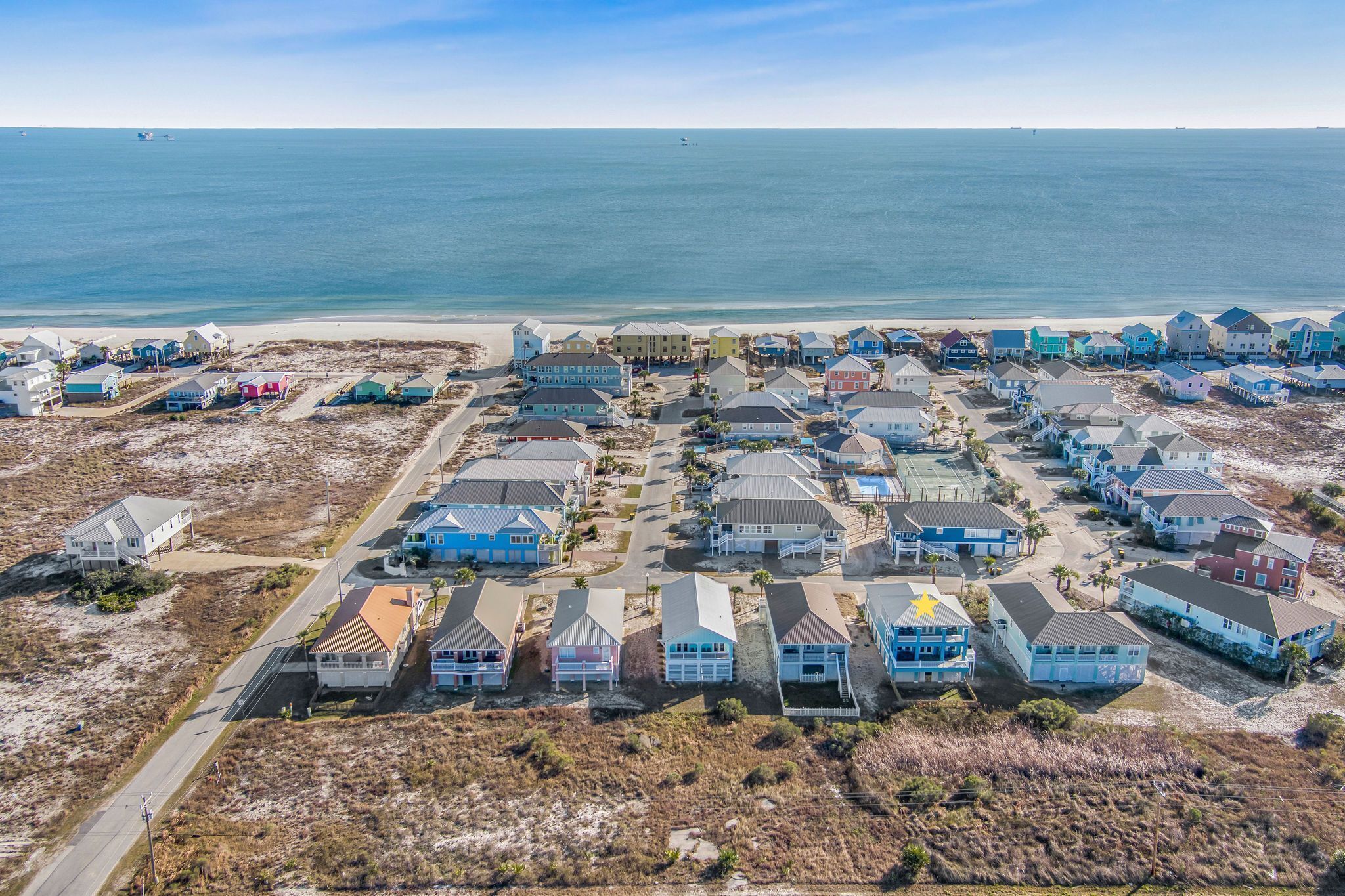 An aerial view of a coastal residential area with houses, a beach, and a clear sky.