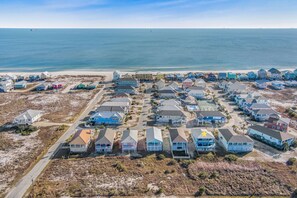 An aerial view of a coastal residential area with houses, a beach, and a clear sky.