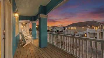 A wooden deck with Adirondack chairs, a railing, and a sunset view.