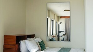 Ein Schlafzimmer mit einem Bett, einem hölzernen Kopfteil, einem Spiegel und einem Fenster.