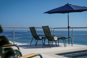 Un terrazza con due sedie, un tavolo, un ombrellone e vista sull'oceano.