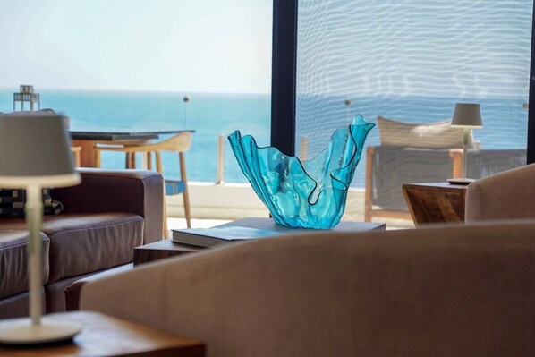 Un salon moderne avec vue sur la mer, une sculpture en verre et un coin salon confortable.