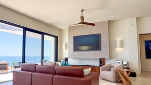Ein modernes Wohnzimmer mit großem Flachbildfernseher, Deckenventilator und Meerblick.
