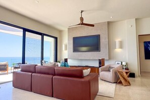 Un soggiorno moderno con una grande televisione a schermo piatto, una ventola a soffitto e vista sull'oceano.