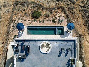 Vue aérienne d’un espace piscine sur le toit, avec des chaises longues et des parasols, le tout entouré d’un paysage rocheux.