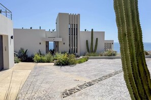 A modern building with a flat roof, a central entrance, and a paved courtyard with patterned tiles.
