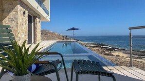 Un espace aménagé au bord de la piscine, avec vue sur l’océan, un mur en pierre et un fauteuil de relaxation.