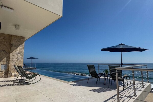 A balcony with a pool, lounge chairs, and a view of the ocean. - Luxe Oceanfront Casita • Pool• Spa• Secluded Beach (La Paz)