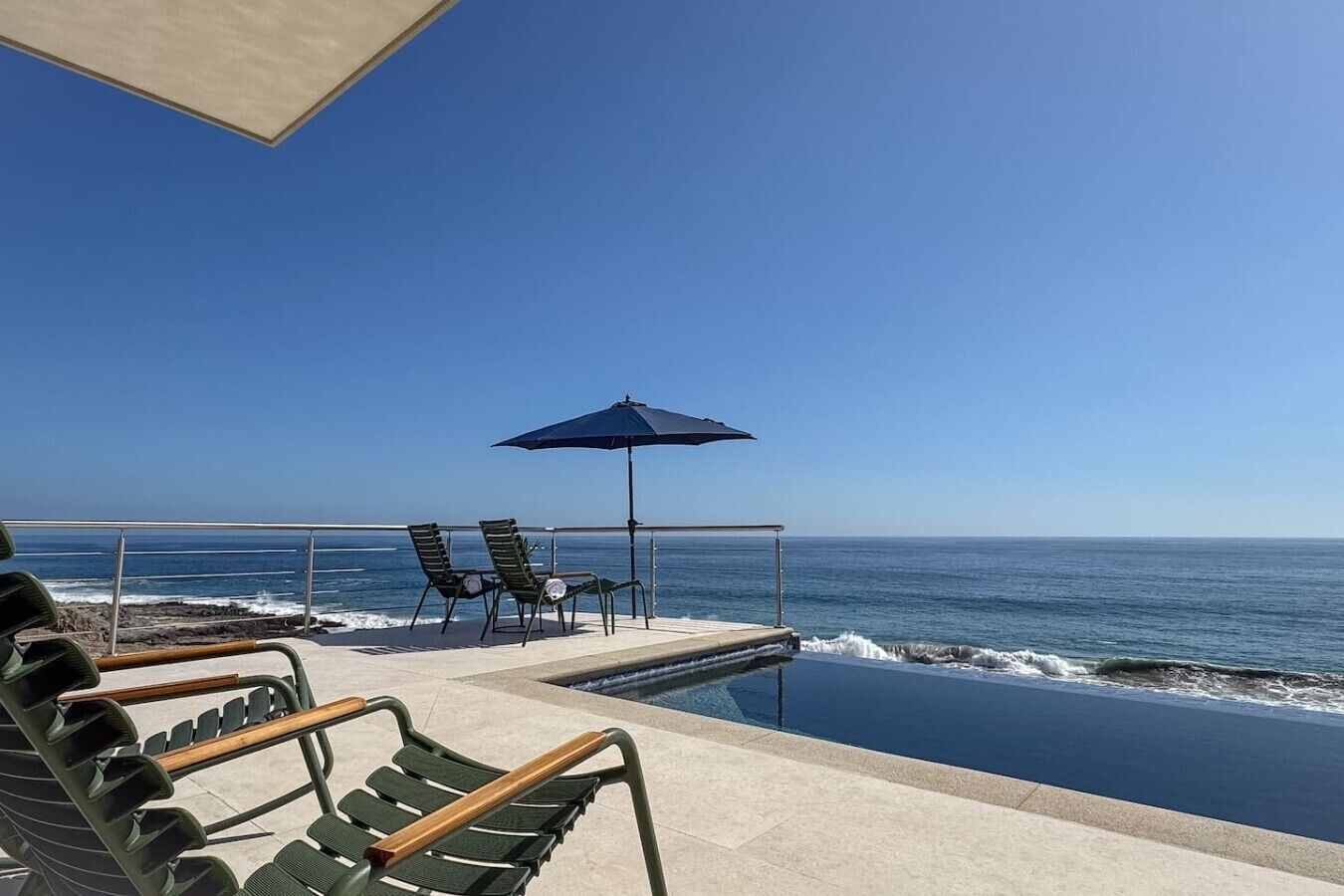 A poolside area with lounge chairs and an umbrella, overlooking the ocean.