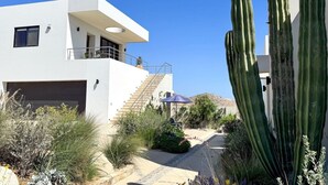 Un bâtiment moderne à deux étages, doté d’un toit plat, d’un escalier menant à l’étage supérieur et d’un espace jardin agrémenté de cactus et de plantes désertiques.