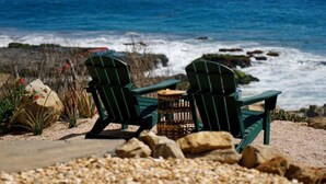 Deux chaises Adirondack vertes, placées face à une côte rocheuse, avec l’océan en arrière-plan.