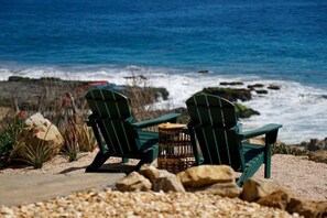Zwei grüne Adirondack-Stühle blicken auf eine felsige Küste mit dem Meer im Hintergrund.