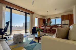 A modern living room with a sofa, a coffee table, and a view of the ocean through large windows. - Luxe Oceanfront Casita • Pool• Spa• Secluded Beach (La Paz)