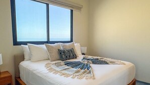 Une chambre d’hôtel avec un lit, des oreillers, un plaid, une table de chevet et une fenêtre donnant sur un beau paysage.