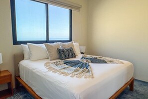 Ein Hotelzimmer mit Bett, Kissen, einer Tagesdecke, einem Nachttisch und einem Fenster mit Blick.