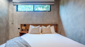 Een slaapkamer met een groot bed, een houten hoofdbord, een klein nachtkastje en een raam.
