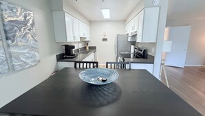 Cozinha moderna com armários brancos, bancada preta e uma mesa de jantar com uma tigela de vidro.