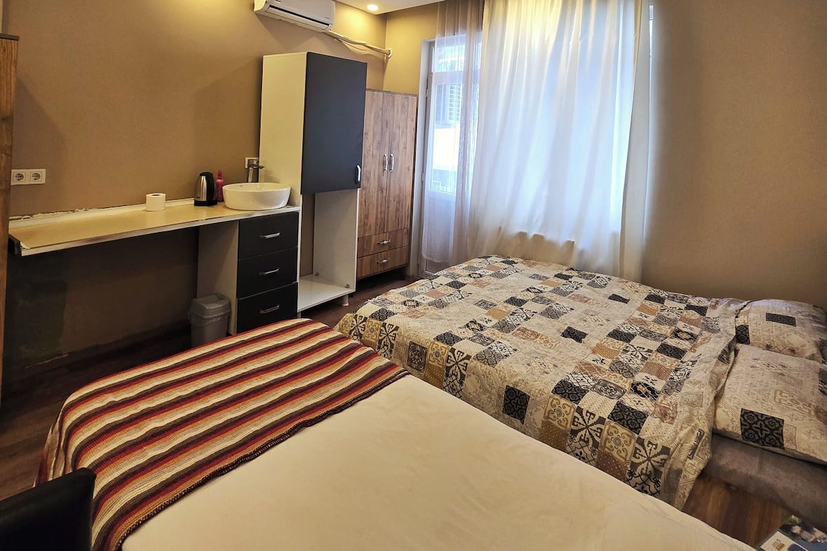 A hotel room with a bed, a desk with a chair, a wardrobe, and a window with curtains.