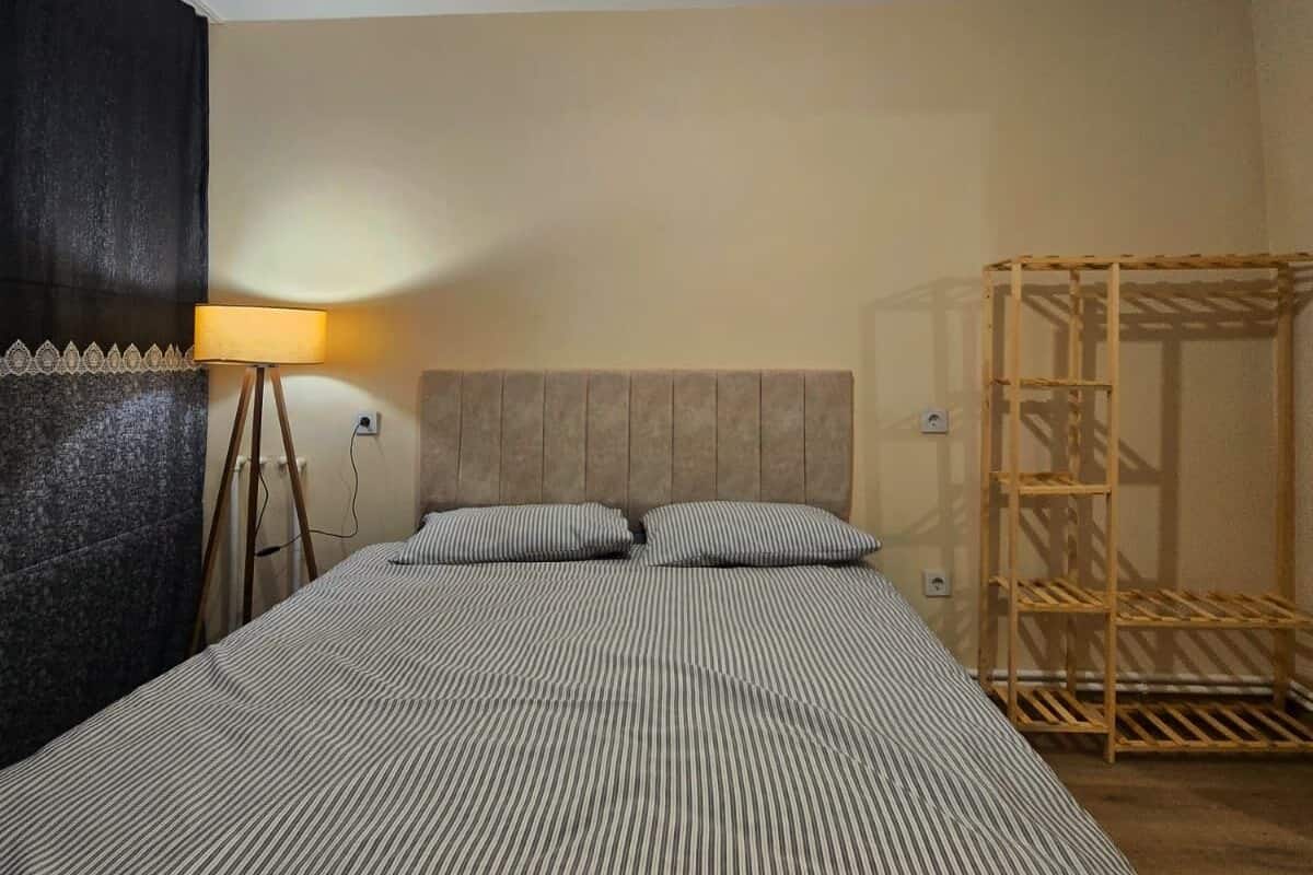 A room with a bed, a standing lamp, and a wooden rack.
