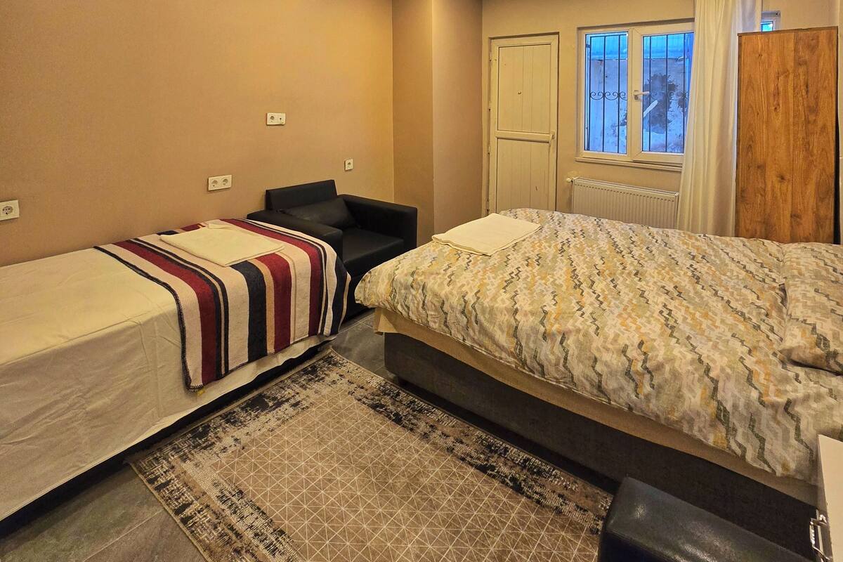 A bedroom with two single beds, a large bed, a window with curtains, and a radiator.