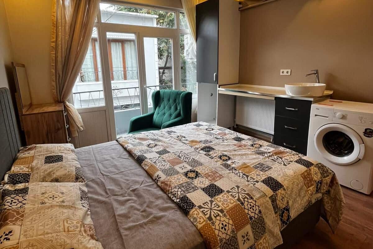 A bedroom with a bed, a chair, a washing machine, and a window with curtains.