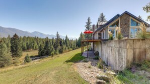 A modern house with a stone facade, a covered porch, and a view of a forest and mountains. - On 160 Acres w/ Creeks & Trails: Scenic Ronan Gem! (Ronan)