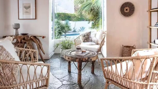 A cozy living room with wicker furniture, a round coffee table, and a view of a tropical garden through a large window. - Palm Springs Oasis • 3 King Ensuites + Pool & Spa (Palm Springs)