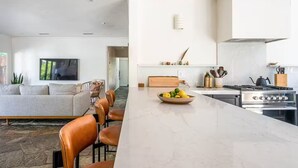 A modern kitchen with a marble countertop, stainless steel appliances, and a dining area with leather chairs. - Palm Springs Oasis • 3 King Ensuites + Pool & Spa (Palm Springs)