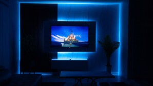 A modern living room with a flat-screen TV mounted on a wall, a potted plant, and a minimalist design. - Family Oasis! Luxe 5BD/4.5BA Townhouse w/Private pool, Disney Proximity (Kissimmee)