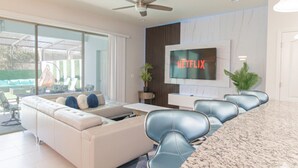 A modern living room with a sofa, chairs, a TV, and a large window. - Family Oasis! Luxe 5BD/4.5BA Townhouse w/Private pool, Disney Proximity (Kissimmee)