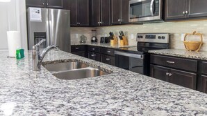 A modern kitchen with dark cabinets, stainless steel appliances, granite countertops, and a double sink. - Family Oasis! Luxe 5BD/4.5BA Townhouse w/Private pool, Disney Proximity (Kissimmee)