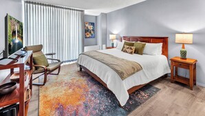 A hotel room with a bed, a desk, a chair, a TV, a painting, and a colorful rug. - Hilo Lagoon Center (Hilo)