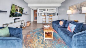 A modern living room with a blue sofa, a coffee table, and a TV on the wall. - Hilo Lagoon Center (Hilo)