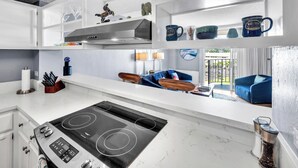 A modern kitchen with white cabinetry, a black stove, and a dining area with a blue sofa and a coffee table. - Hilo Lagoon Center (Hilo)
