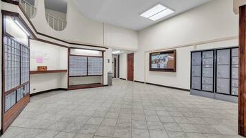 A spacious hallway with a tiled floor, a wooden bench, a bulletin board, and a row of metal lockers.