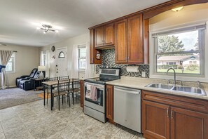 Une cuisine avec des meubles de rangement en bois, une cuisinière, un lave-vaisselle et une fenêtre donnant sur des maisons.
