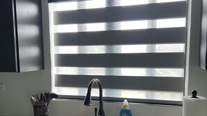 A kitchen with a double sink, a black faucet, a window with blinds, a soap dispenser, and a sponge.