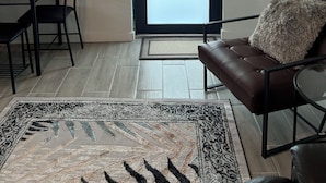 A living room with a brown leather sofa, a dining table with chairs, a patterned rug, and a large frosted glass door.