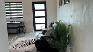 A living room with a black leather sofa, a potted plant, a dining area with a table and chairs, and a ceiling fan.