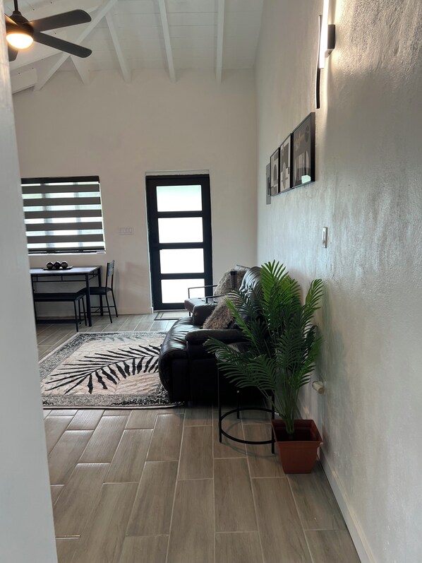 A living room with a black leather sofa, a potted plant, a dining area with a table and chairs, and a ceiling fan.