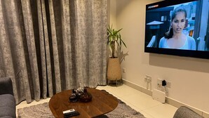 A living room with a wooden coffee table, a TV mounted on the wall, a potted plant, and a grey sofa. - Chic 1-bedroom apartment at The Lennox, Airport Residential Area (Accra)