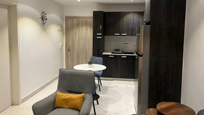 A modern kitchen with dark cabinetry, a white countertop, and a built-in oven. There is a dining area with a round table and two chairs. - Chic 1-bedroom apartment at The Lennox, Airport Residential Area (Accra)