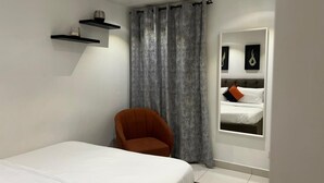A bedroom with a single bed, a chair, a window with curtains, and a mirror reflecting the bed. - Chic 1-bedroom apartment at The Lennox, Airport Residential Area (Accra)