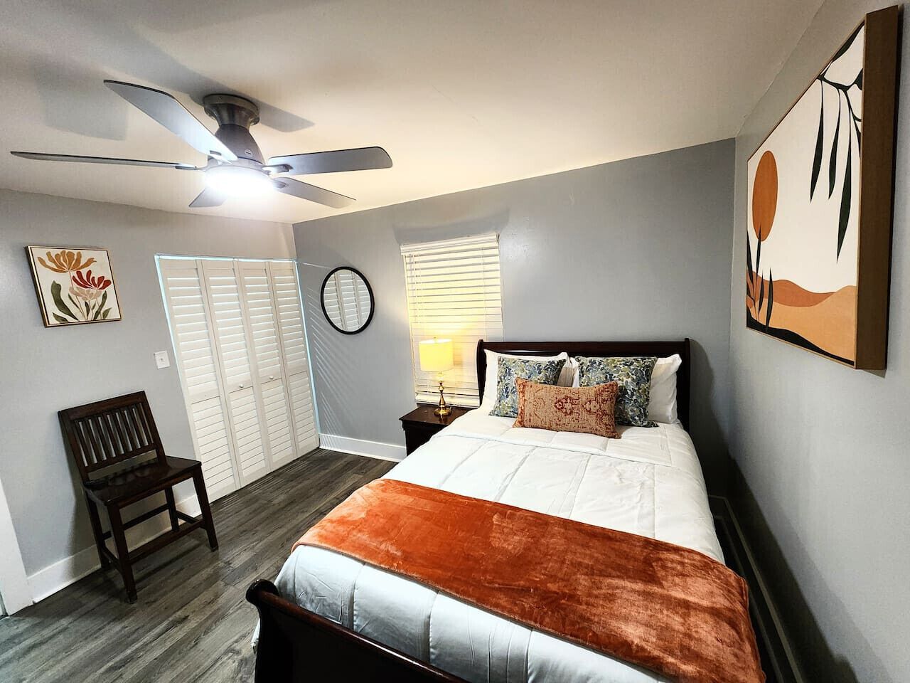 Ein Schlafzimmer mit Bett, Stuhl, Deckenventilator, Fenster mit Jalousien und einer Wanduhr.