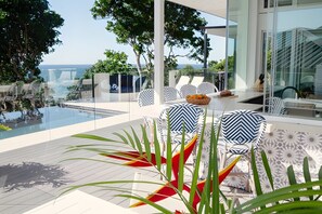Un espace piscine extérieur moderne, doté de chaises longues et offrant une vue sur la mer.