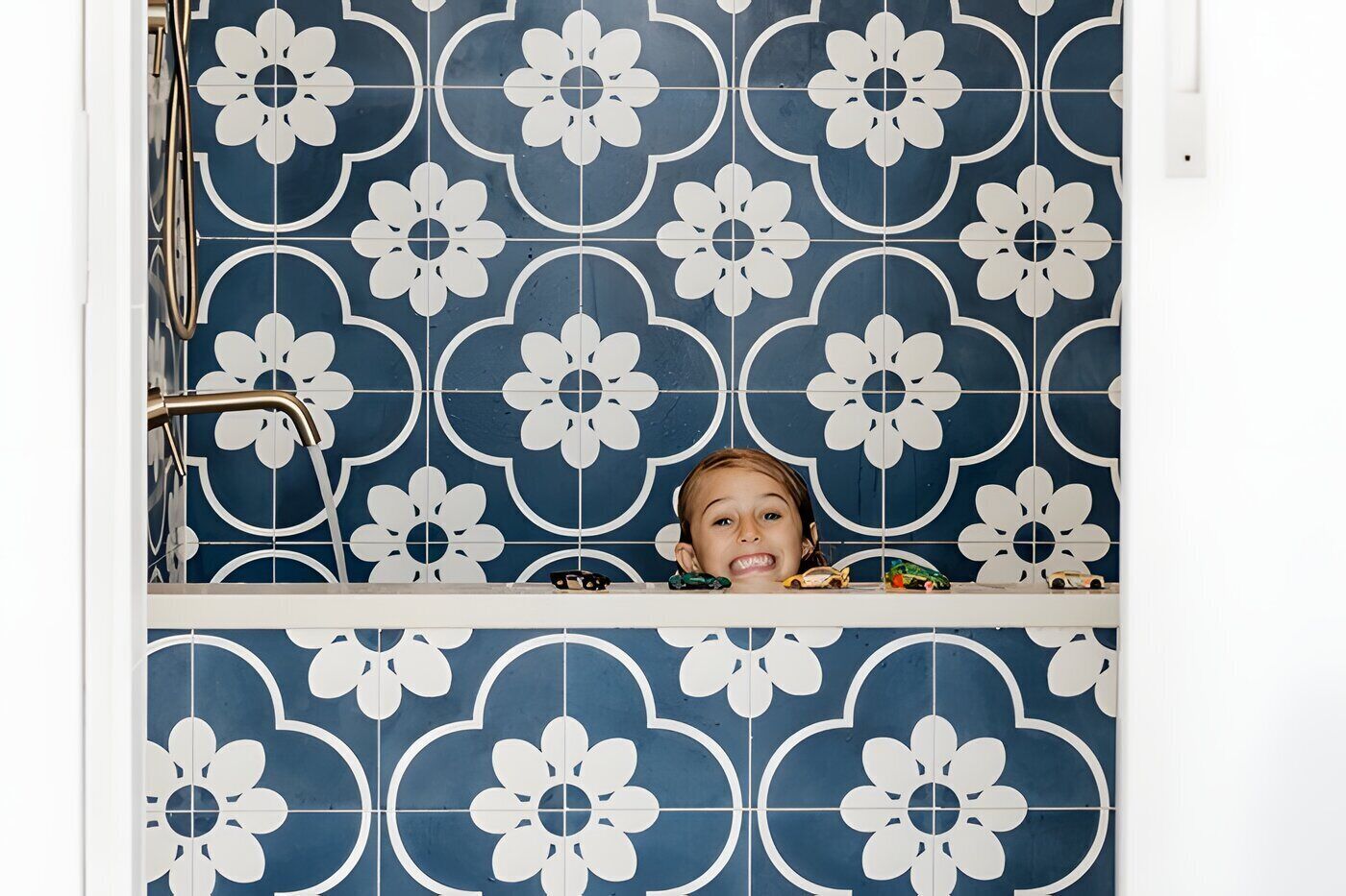 A bathroom with blue and white floral tiles, a shower area, and a child in a bathtub.