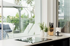 Une cuisine moderne dotée d’une paroi vitrée, d’un plan de travail blanc et offrant une vue sur l’extérieur.