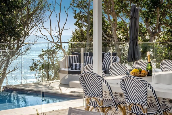 Un espace aménagé au bord de la piscine, avec des sièges d’extérieur, une balustrade en verre et une vue sur la mer.