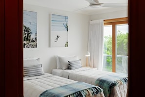 A bedroom with two beds, a ceiling fan, a window with curtains, and artwork on the walls.