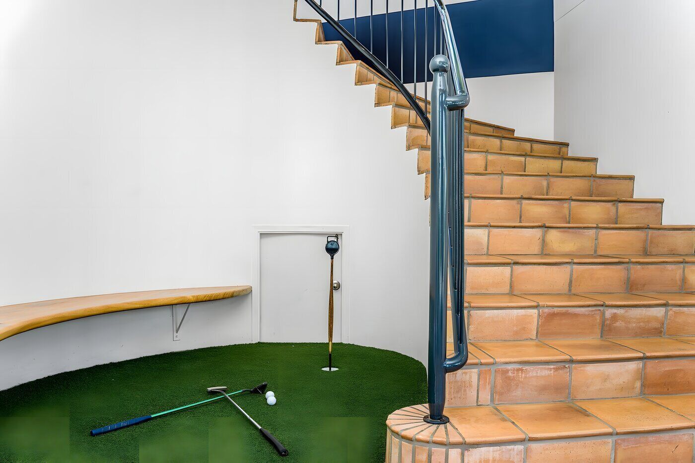 A staircase with a blue handrail, a wooden bench, and a green artificial turf area with golf equipment.